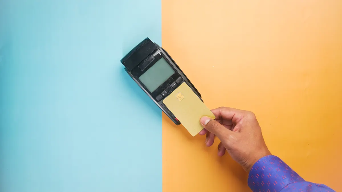 A hand tapping a credit card on a payment terminal for a contactless transaction.