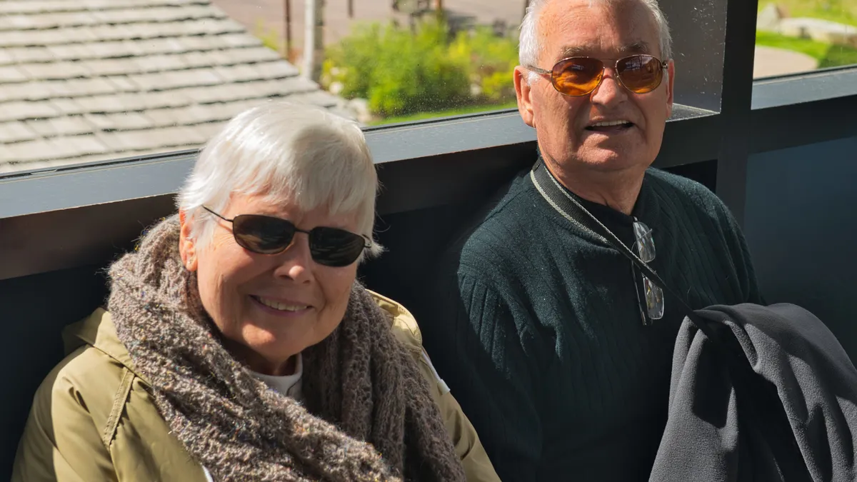 A happy senior couple wearing sunglasses and smiling, enjoying a sunny day outdoors.