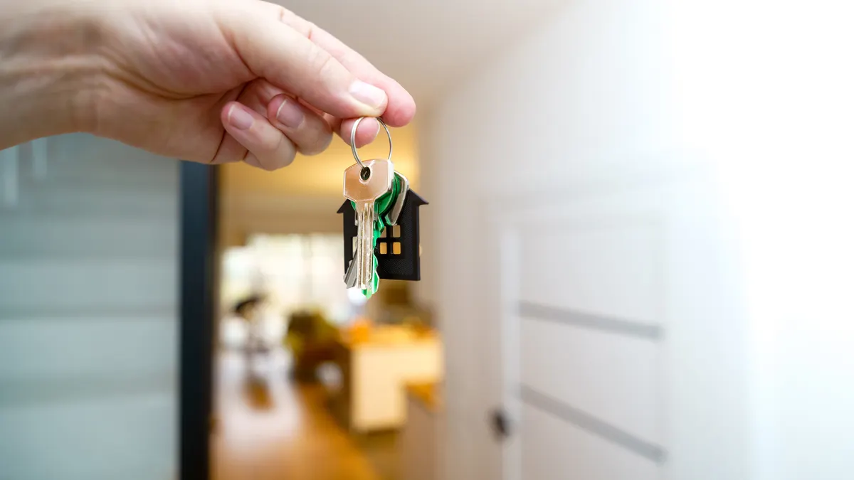 A hand holding house keys inside a modern apartment, symbolizing new property ownership or rental.