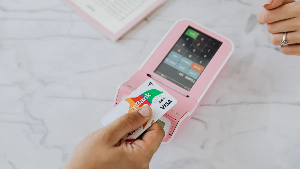 Hand using a contactless card on a pink POS terminal for a wireless transaction.
