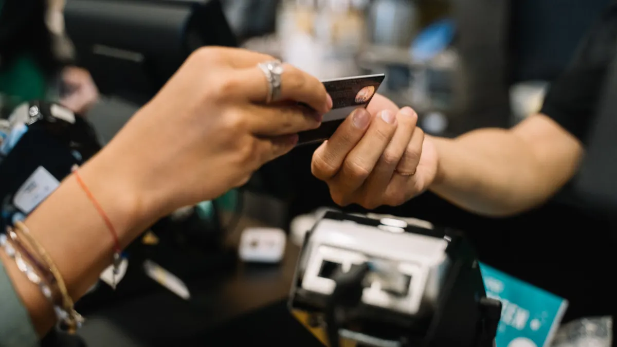 Close-up of hands completing a payment transaction at a retail checkout using a bank card.