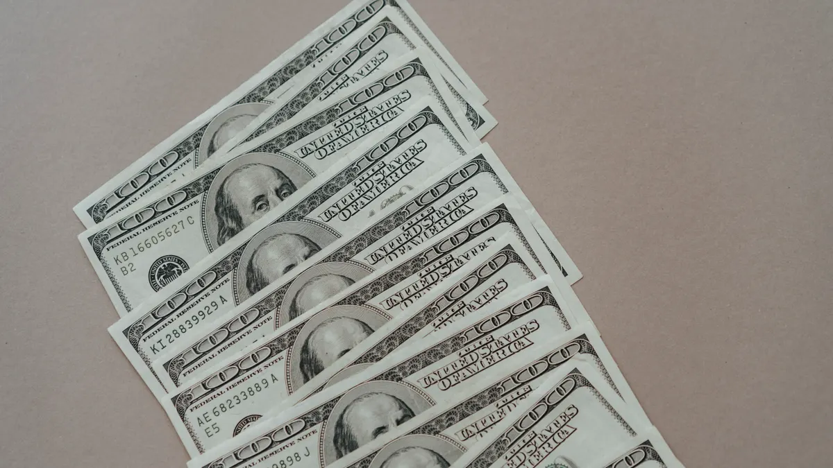 A close-up of multiple US dollar bills arranged on a neutral surface.