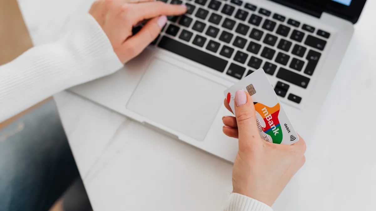 Close-up of a person using a laptop and holding a credit card for online shopping.