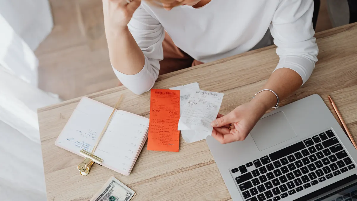 Woman reviewing receipts and planning budget using a laptop and notebook at home to manage expenses.