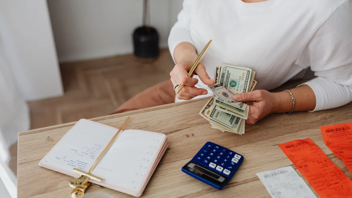 Woman sorting finances with a calculator, cash, and receipts at a desk.