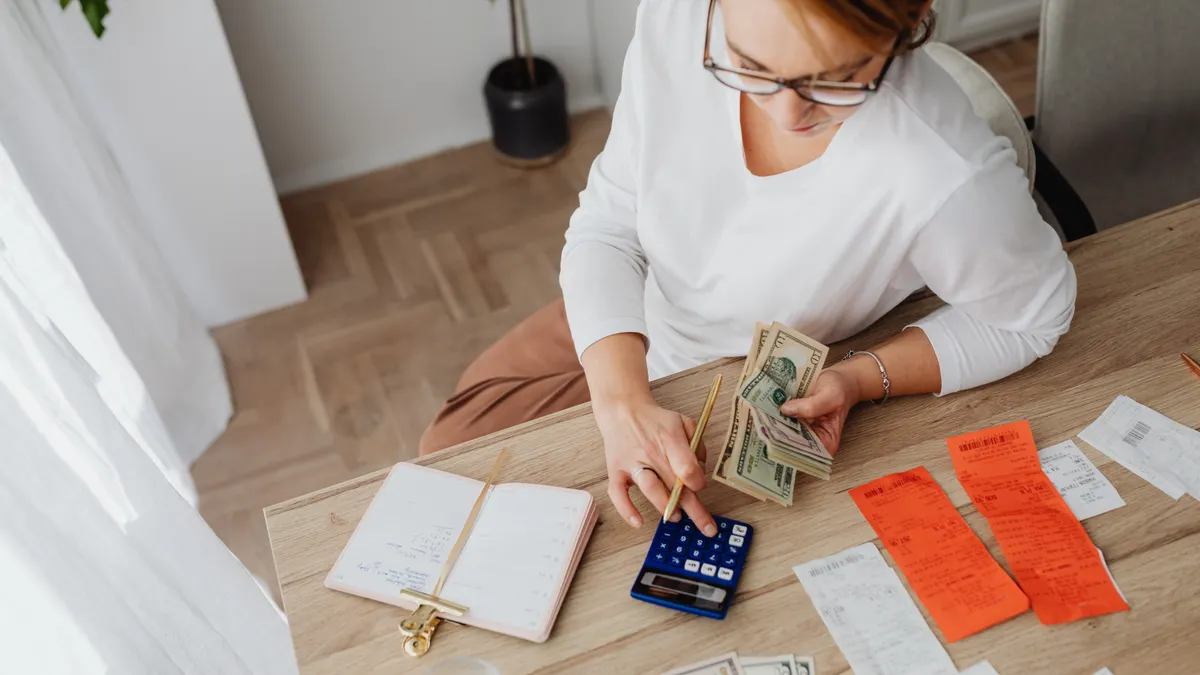 Top view of a woman managing finances with a calculator, cash, and bills in a home setting.