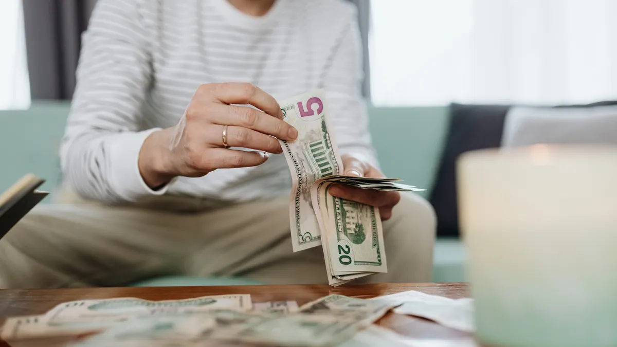 Close-up of hands counting dollar bills indoors, offering a personal finance theme.
