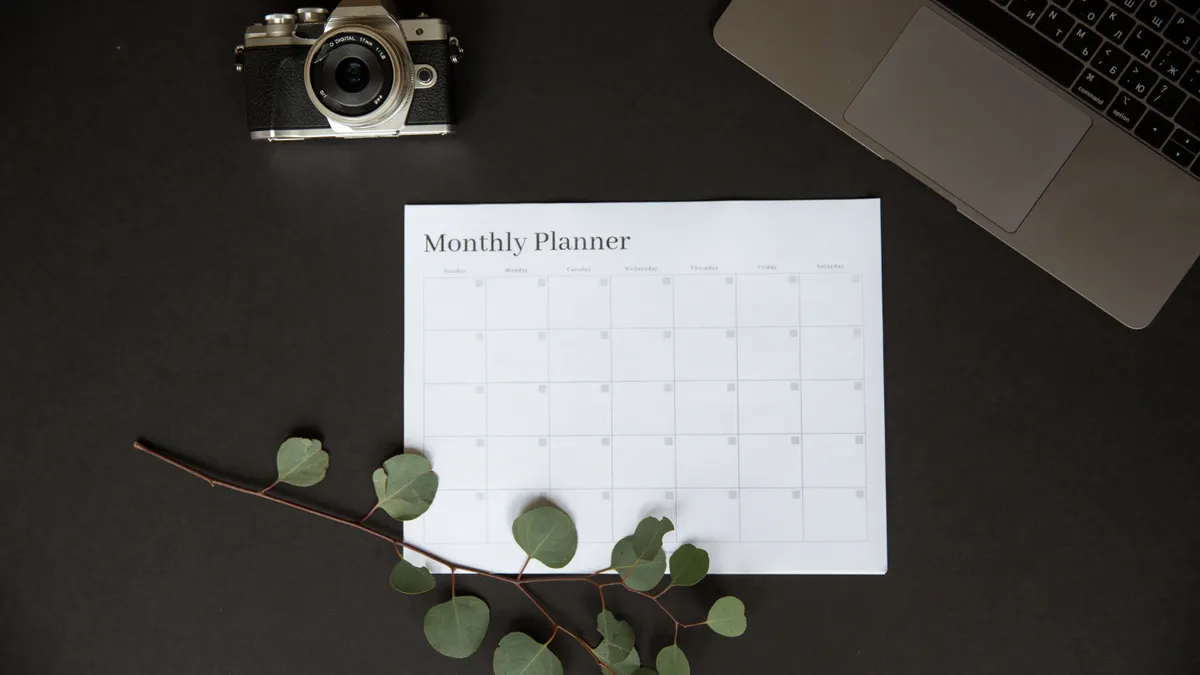 Flat lay of a monthly planner beside a camera and laptop for productivity.