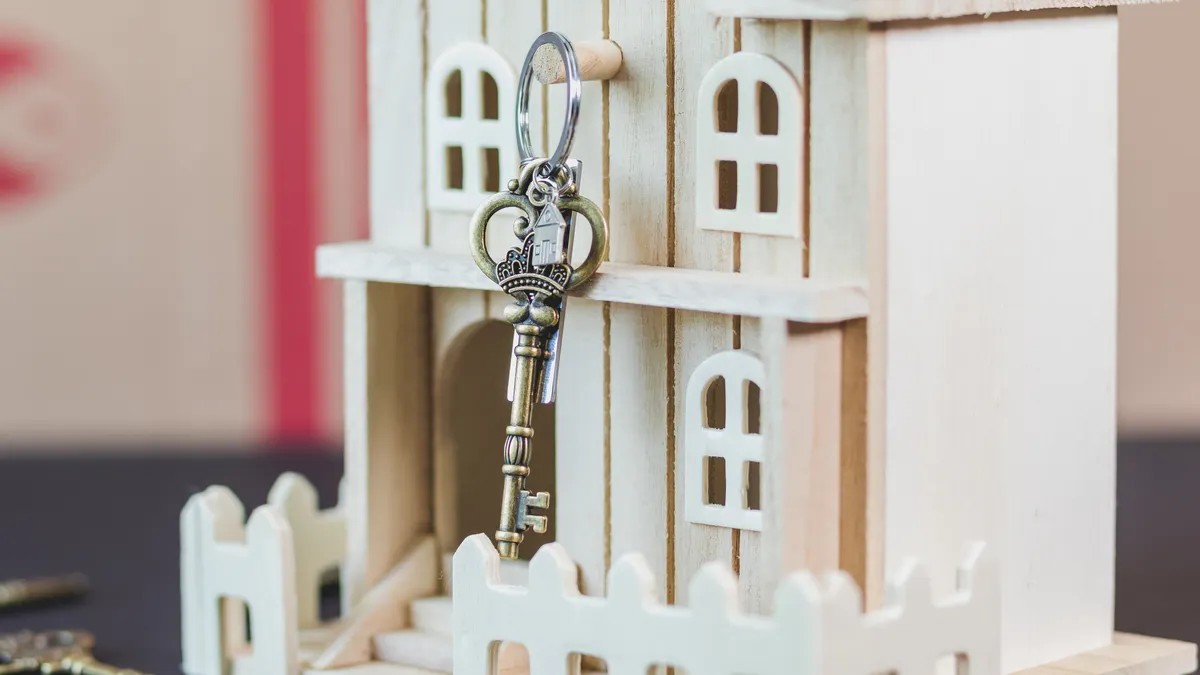 Miniature wooden house with a vintage key, symbolizing real estate and homeownership.
