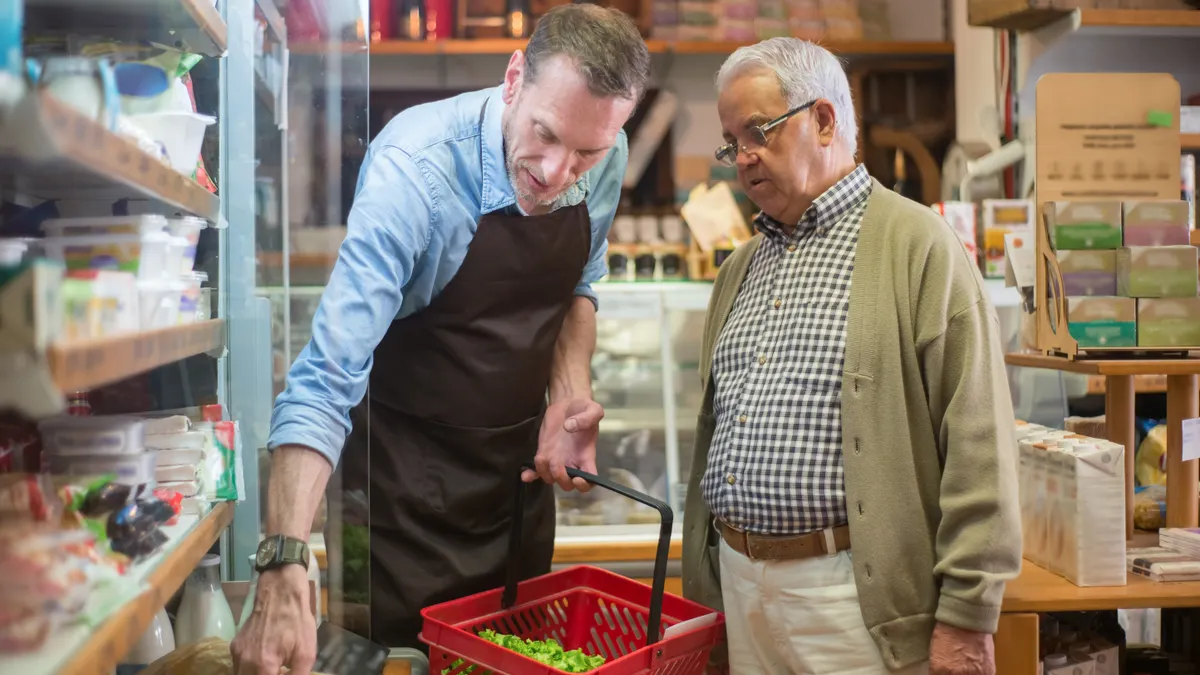 A salesman helps an elderly man with shopping in a local grocery store.