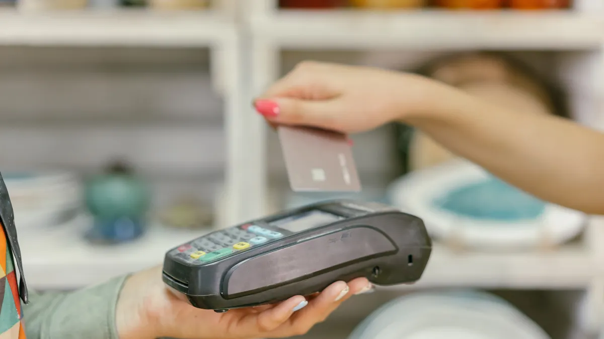 A hand using a credit card for payment at a point of sale terminal, close-up view.